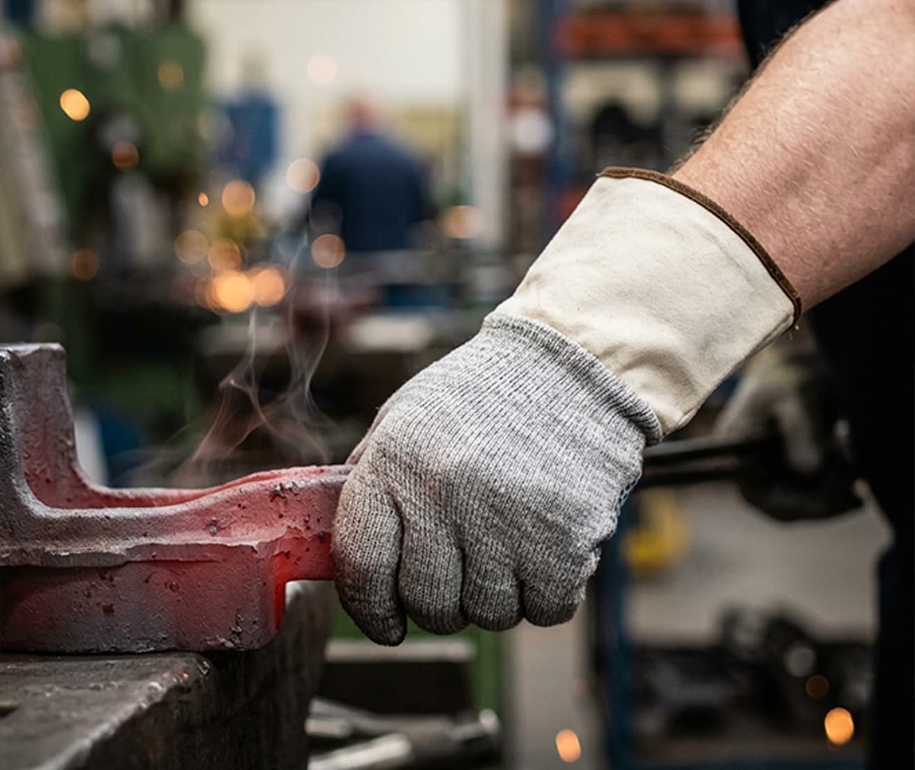 Worker in protective gloves gripping heated metal in a metallurgical workshop